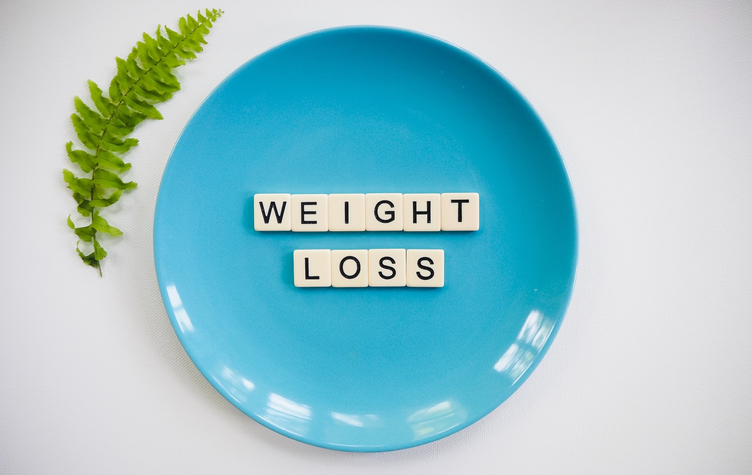 blue plate with word blocks text weight loss on white background with green leaf